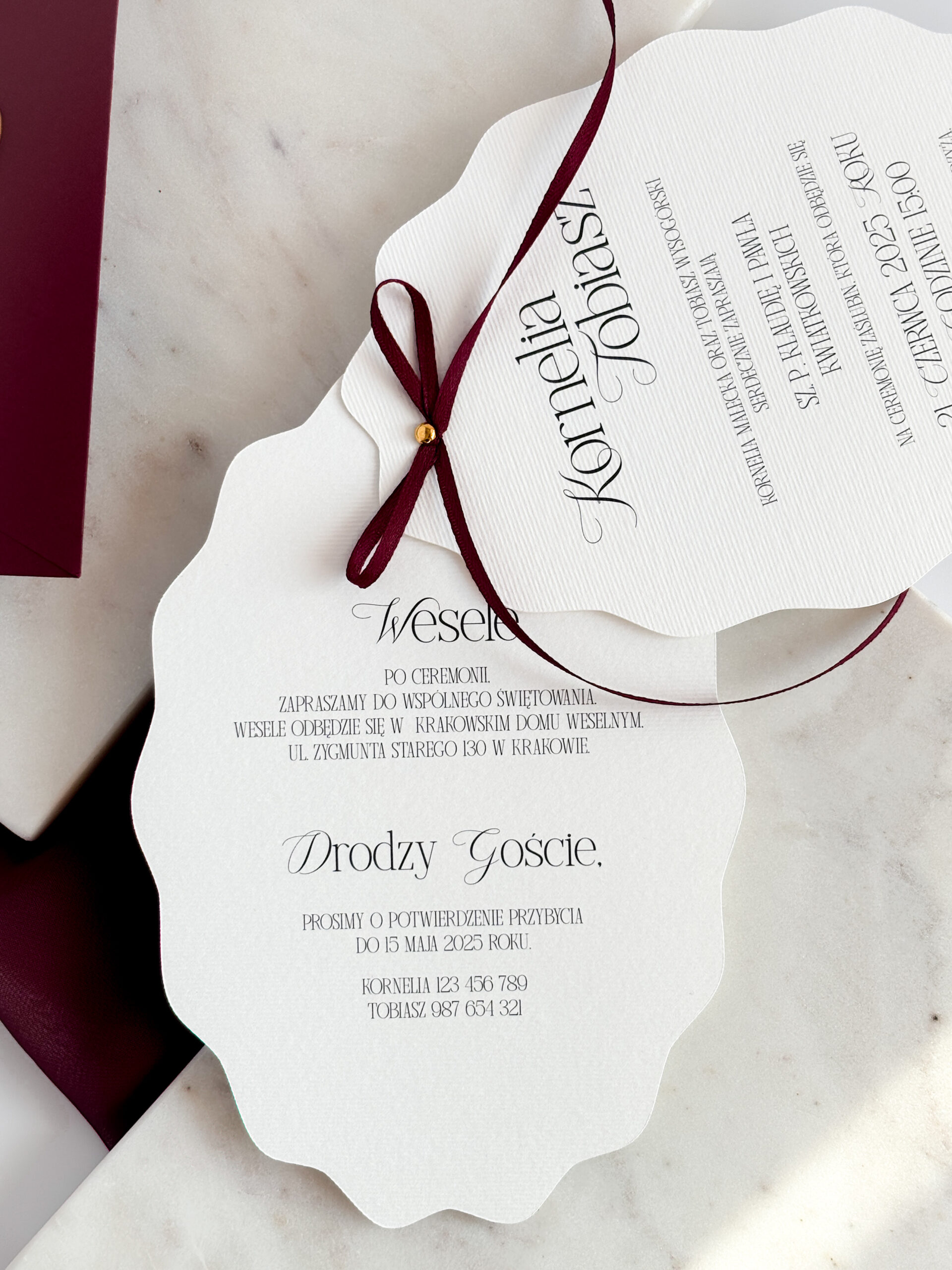rozłożone karty zaproszenia ślubnego spięte złotą pinezką i bordową wstążką