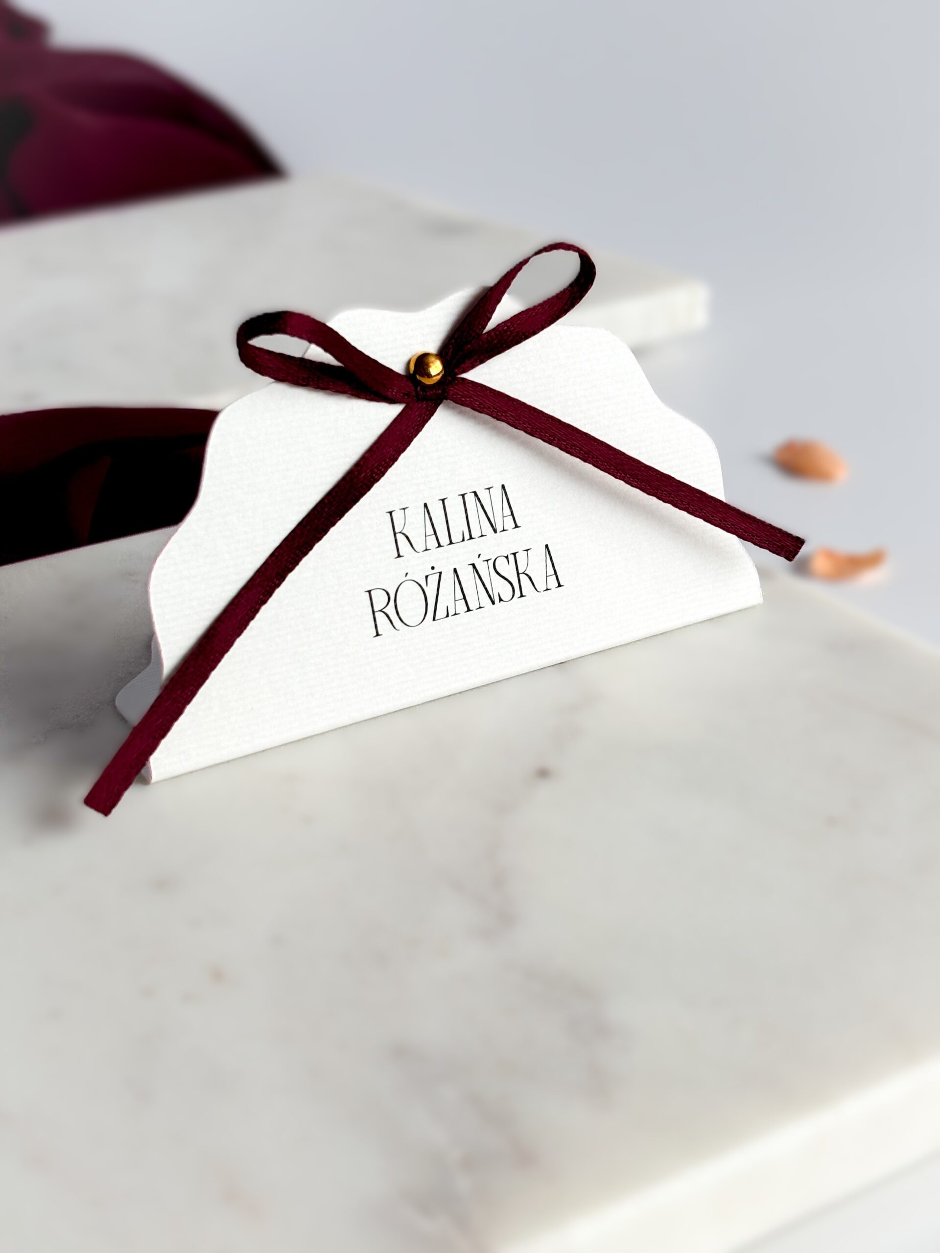 Winietka z kokardką Vivienne – bordowa kokardka i złoty detal Winietka z kokardką – stojąca, biały fakturowany papier, bordowa kokardka, złota pinezka